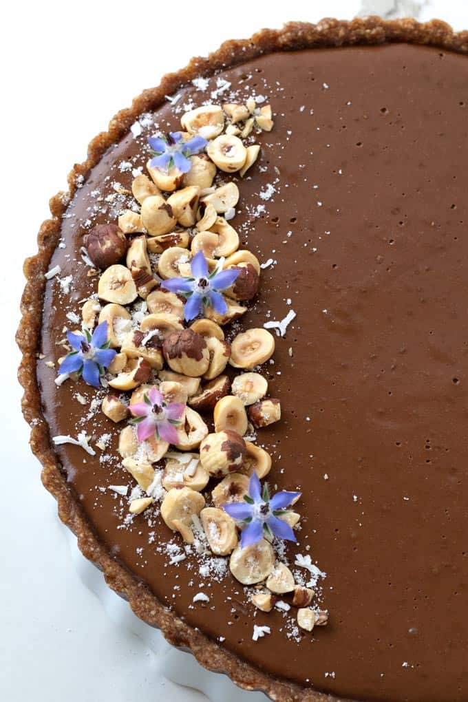 Overhead view of vegan chocolate tart decorated with borage flowers and hazelnuts.