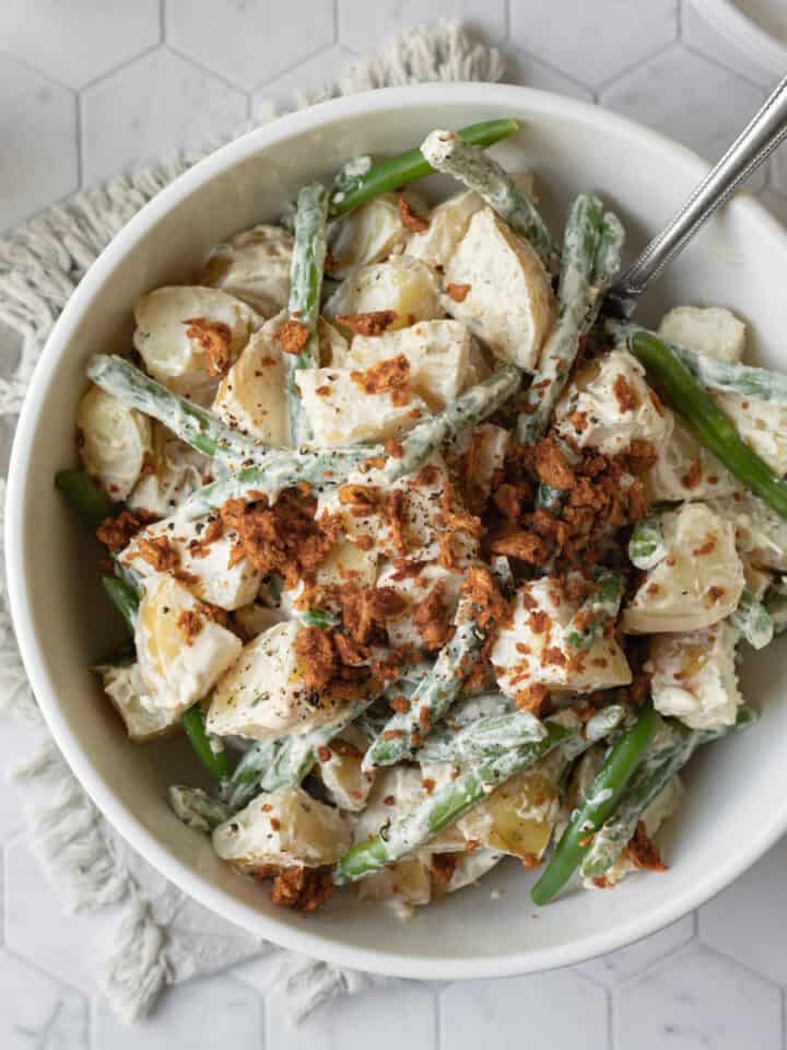 potato salad with green beans and vegan bacon bits in a white serving bowl.
