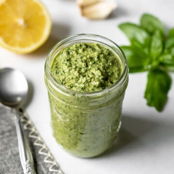 close up of thick basil pesto in a jar on a white countertop.