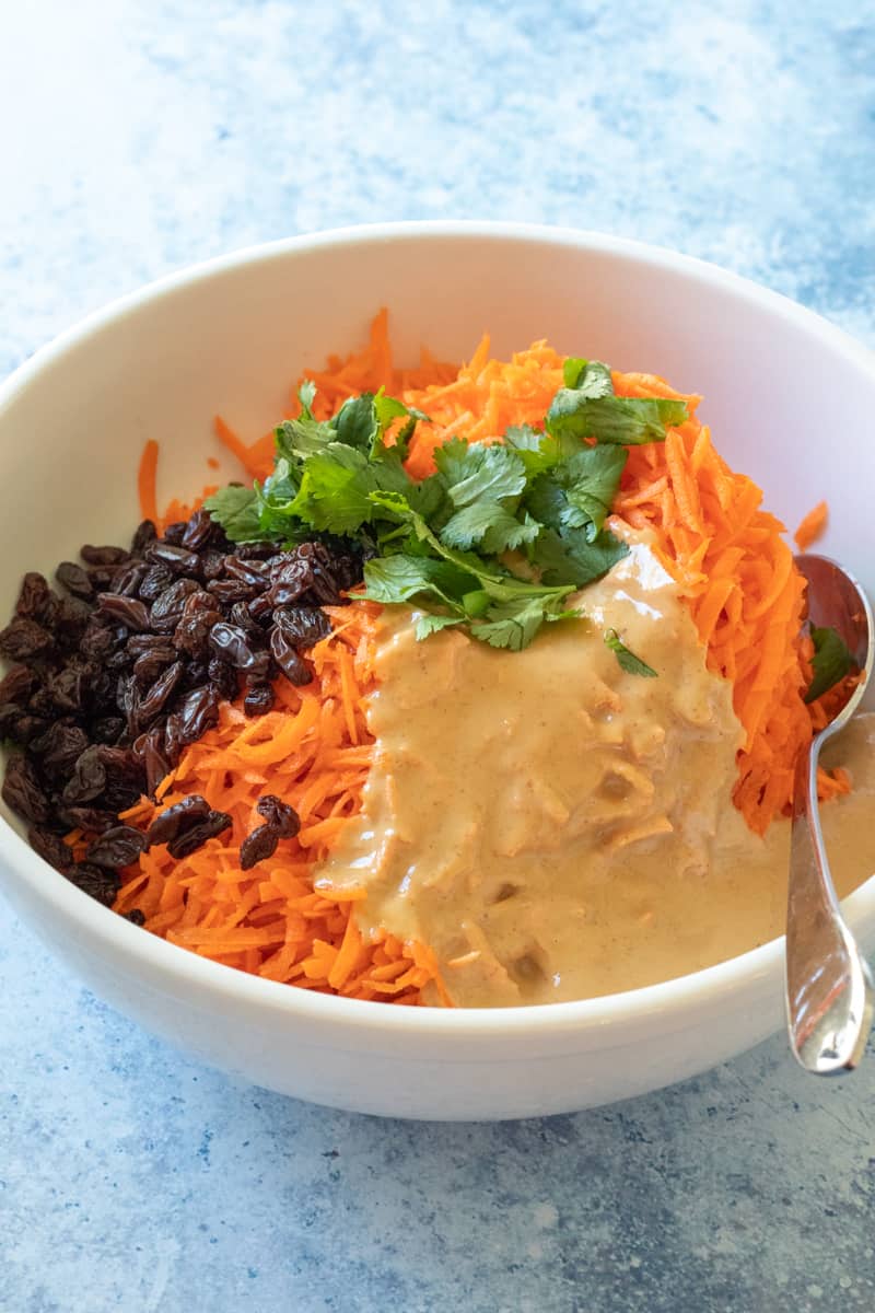 carrots, raisins, tahini dressing, and cilantro in a bowl before mixing.