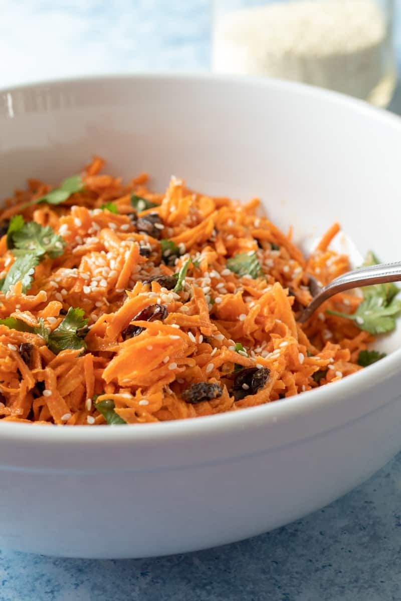vegan carrot salad with raisins and cilantro in a white bowl.