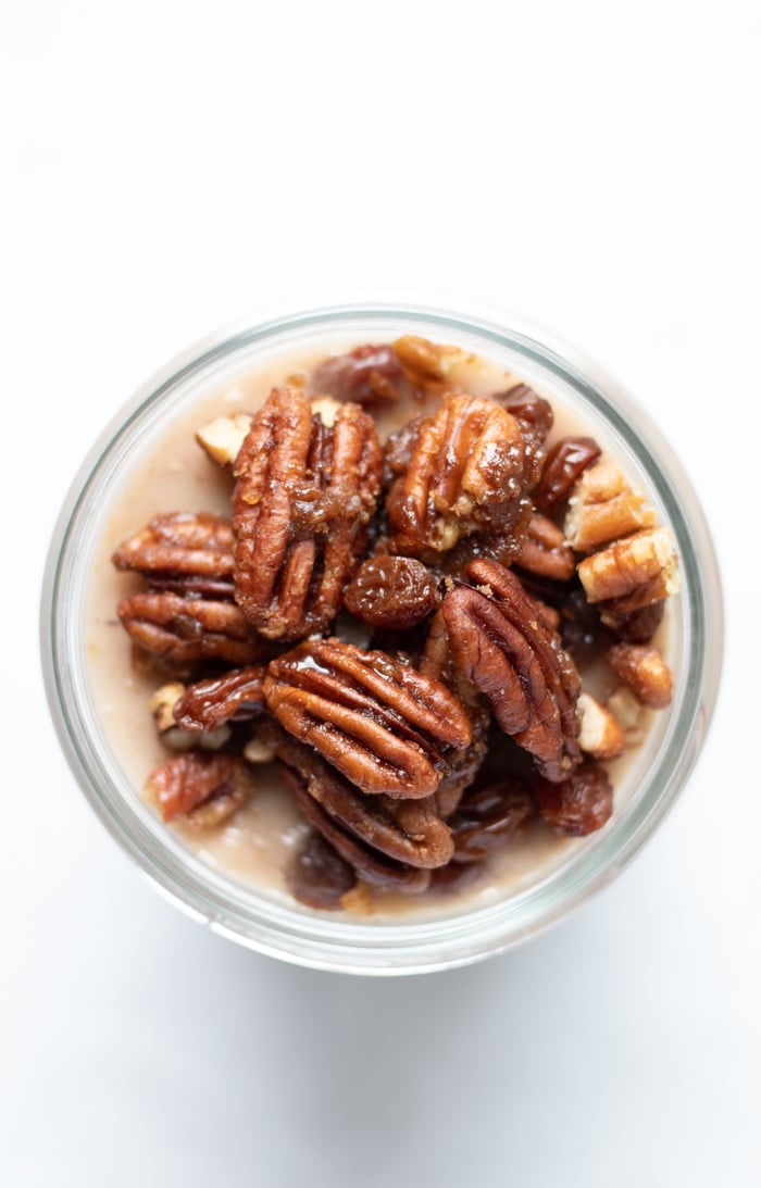 overhead close up showing pecans and raisins piled on top of a jar of pudding