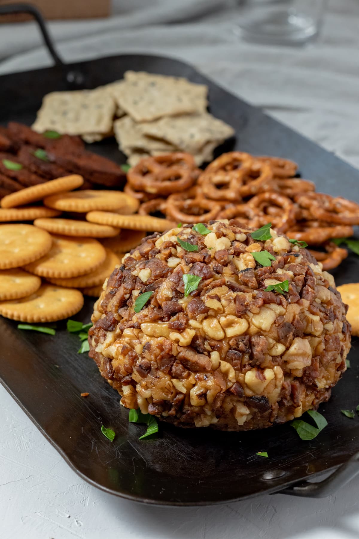 Vegan cheese ball coated with tempeh bacon and walnuts sitting on a platter.