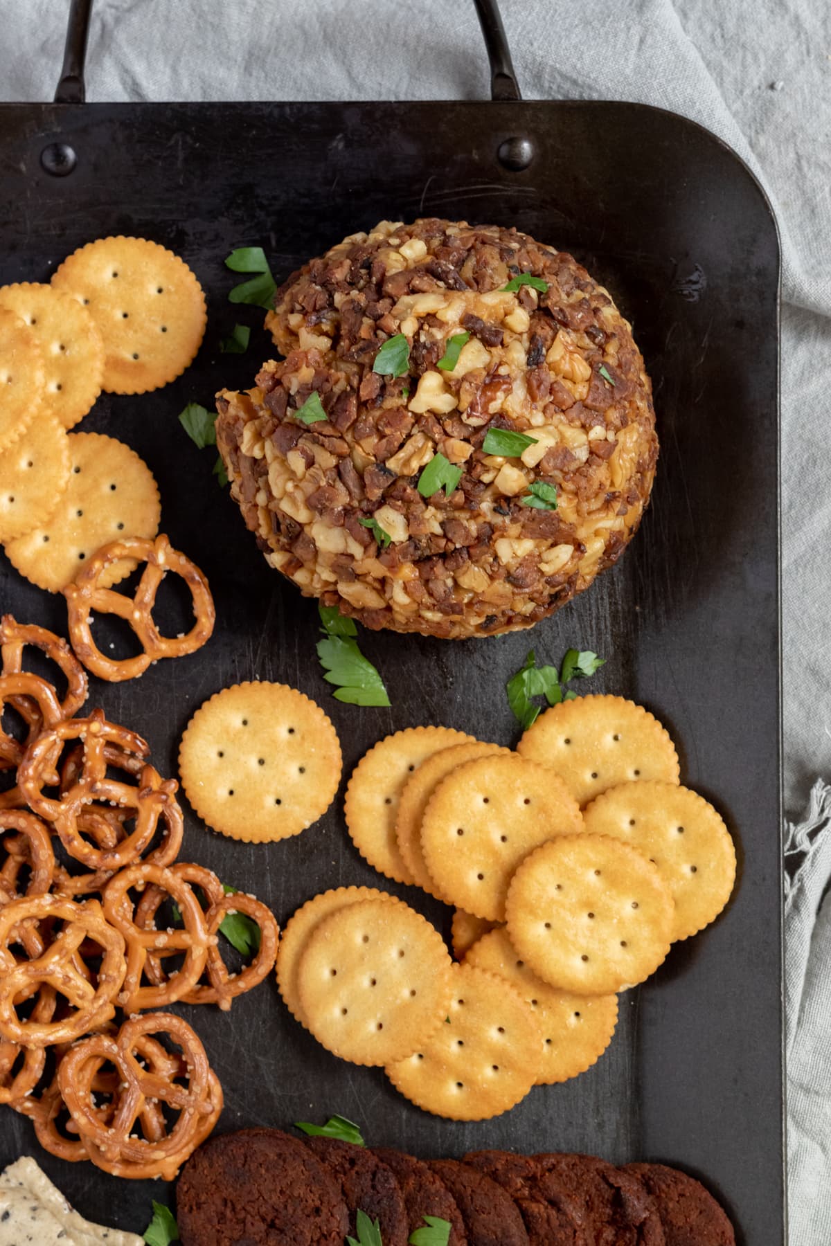 vegan cheese ball on black platter with crackers and pretzels.