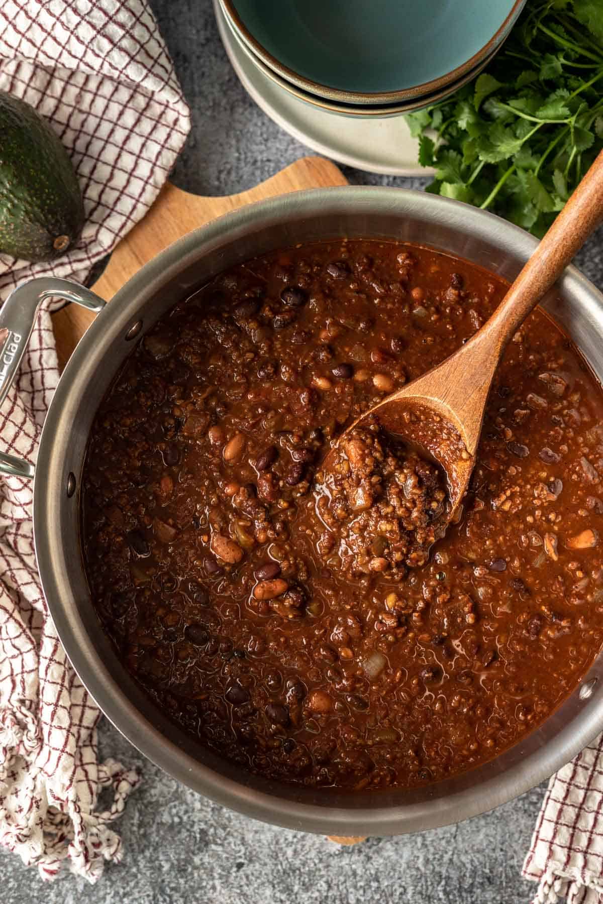 a wooden spoon dipping into a large pot full of thick vegan chili.