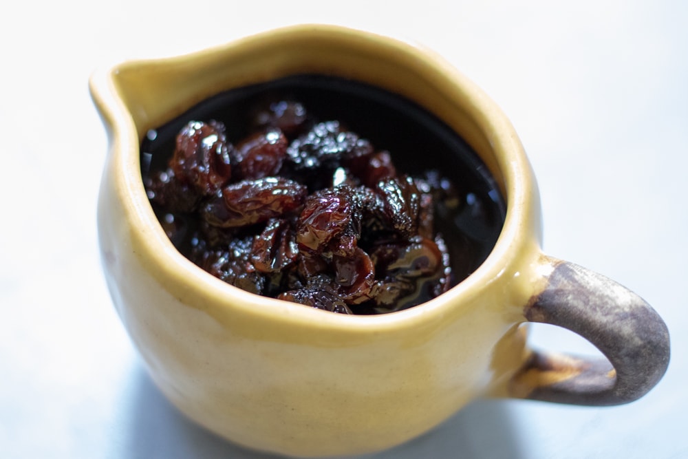 Raisin balsamic reduction in a small yellow gravy boat.