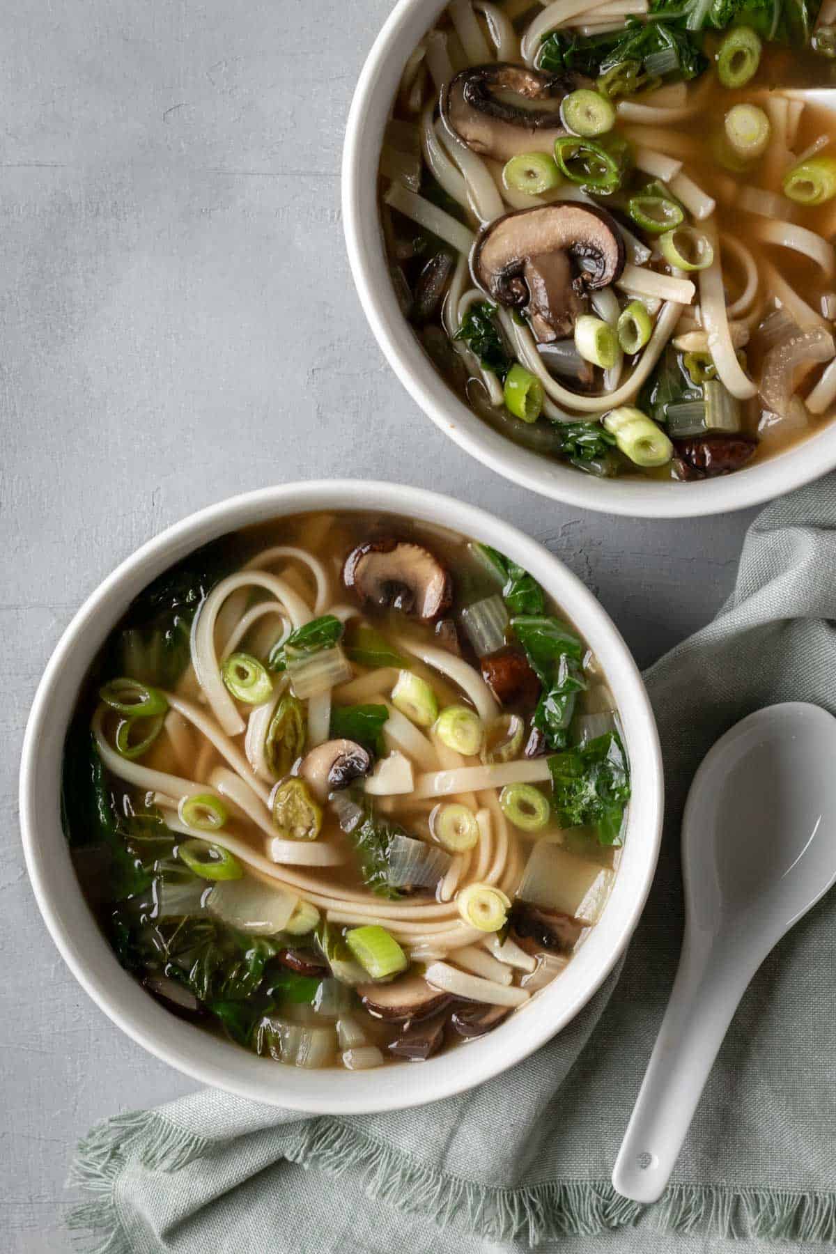 Two bowls of noodle and bok choy soup against a gray background.