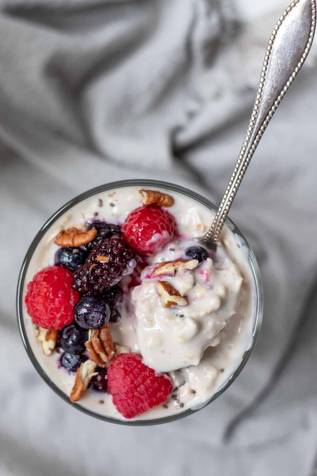 A spoon scooping up creamy oats with yogurt with mixed berries and chopped pecans.