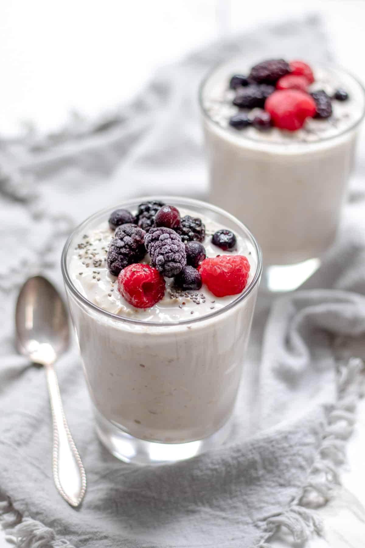 two glasses filled with creamy overnight oats with yogurt, topped with berries.