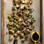 Pan-seared and roasted Brussels spread on a pan and drizzled with dark and thick balsamic reduction.