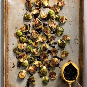 Pan-seared and roasted Brussels spread on a pan and drizzled with dark and thick balsamic reduction.