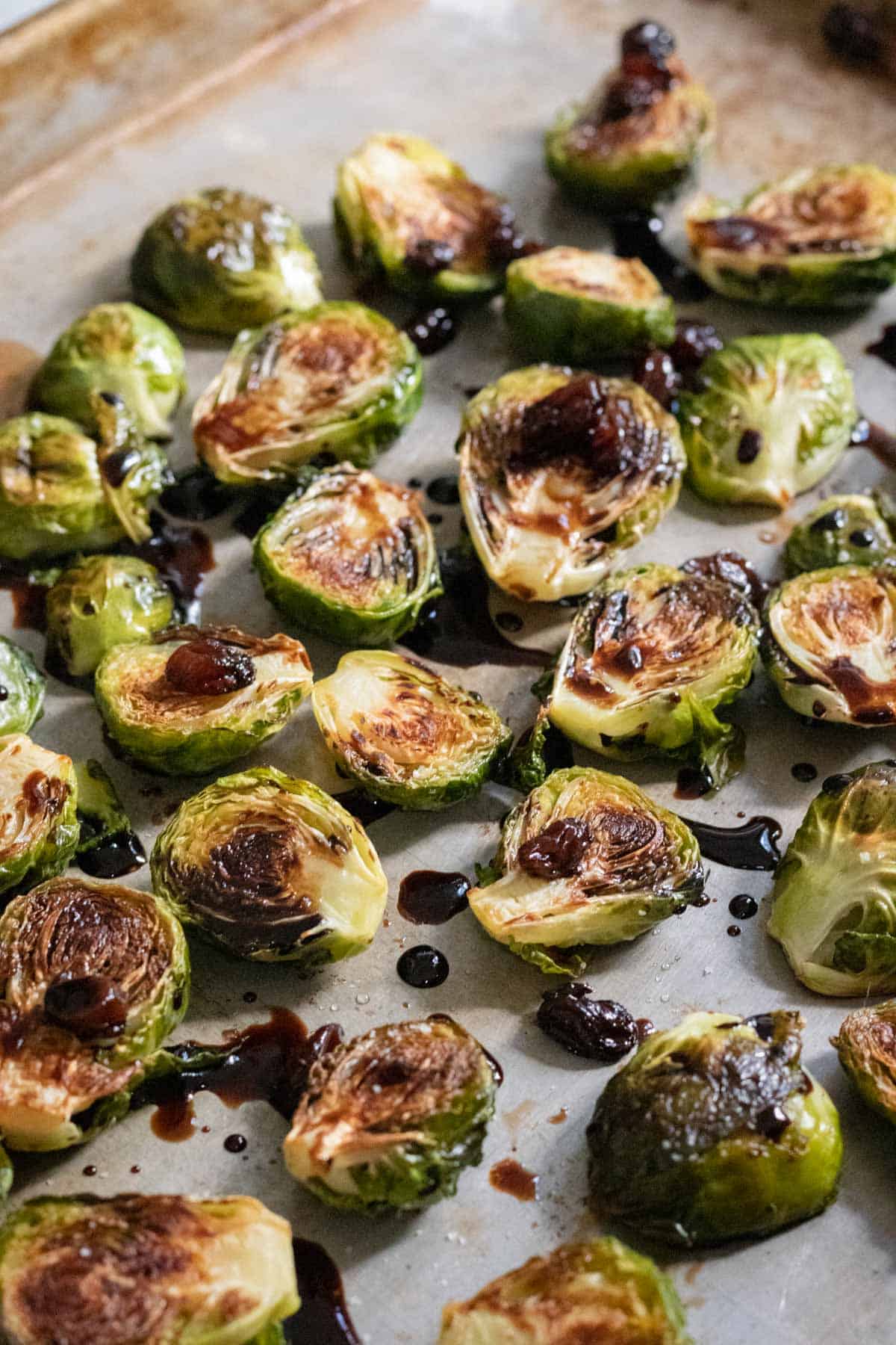 Seared Brussels sprouts drizzled with balsamic reduction and spread out on a large pan.