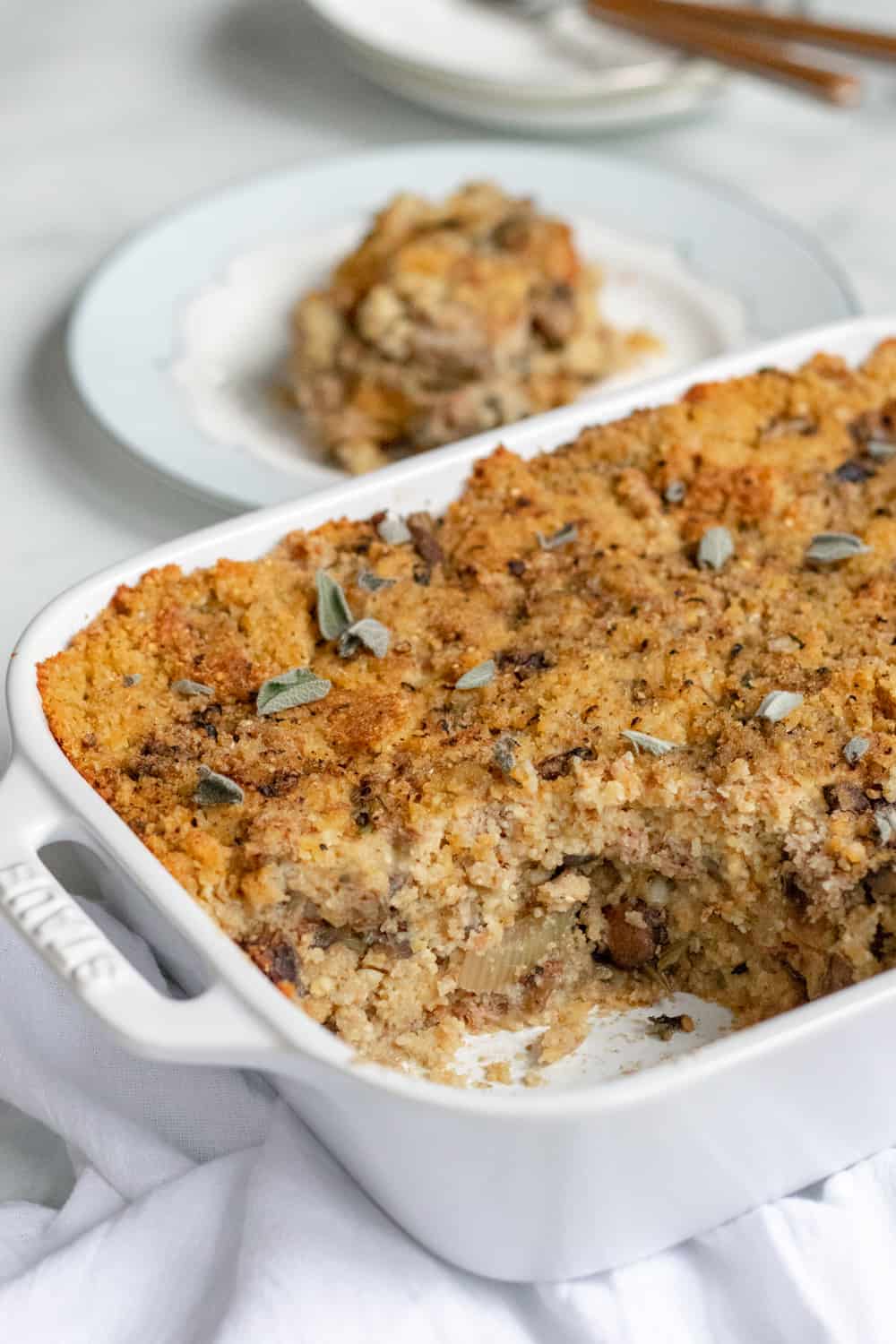 moist vegan cornbread dressing garnished with sage in a white baking dish.