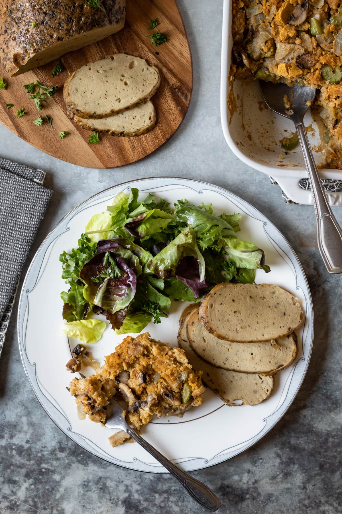 Thanksgiving meal on a plate, with vegan dressing, seitan turkey, and salad.