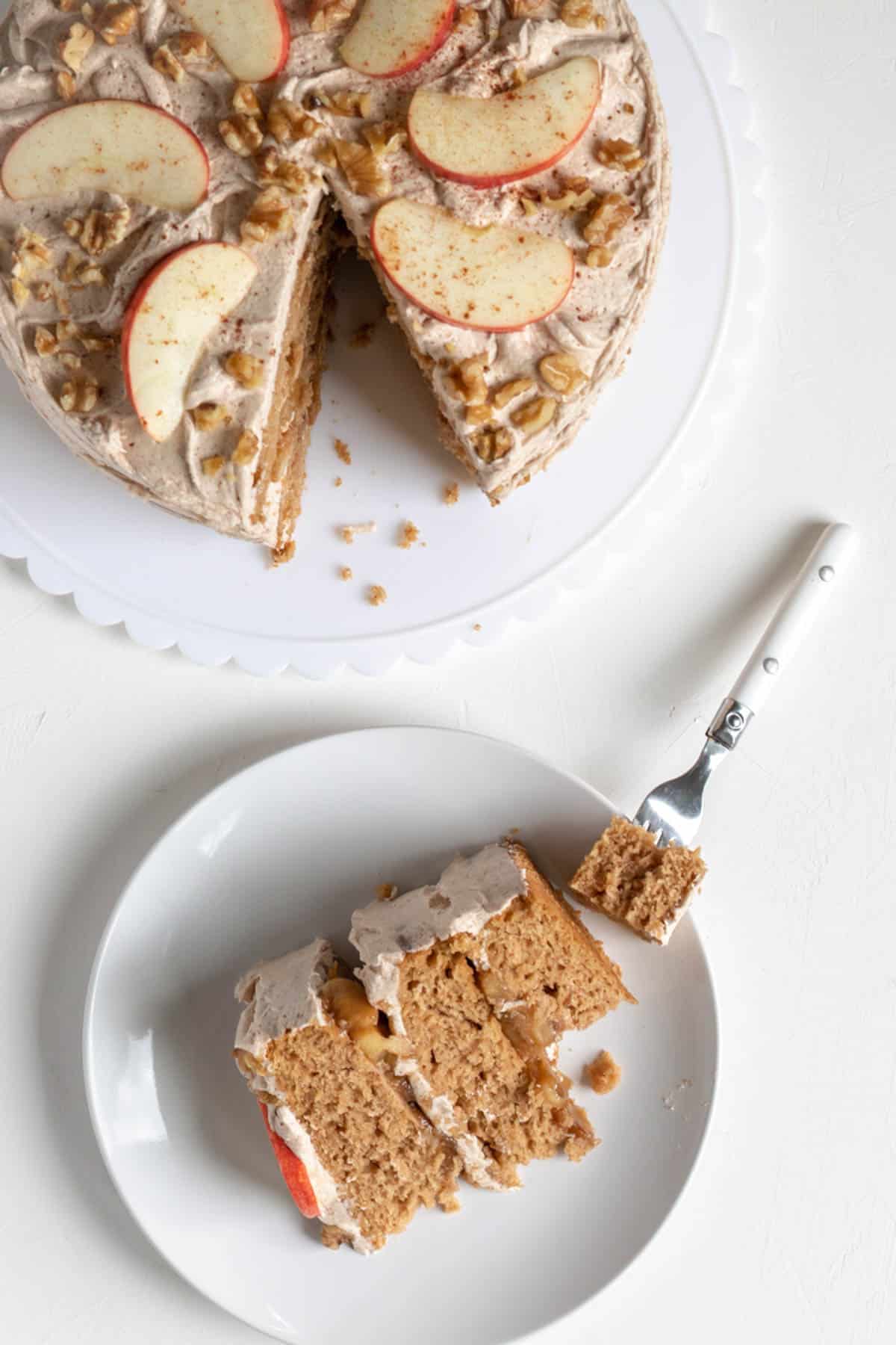 a slice of apple layer cake on a plate with a bite on a fork and the whole cake next to the plate.