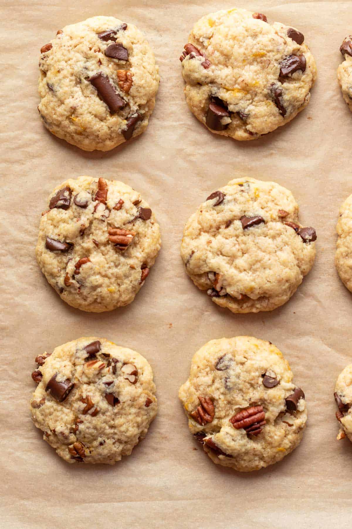 Cookies with big chunks of chocolate and pecans on parchment paper.