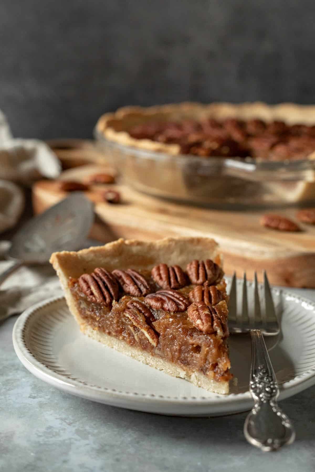 slice of pie and a fork on a plate with whole pie plate in background.