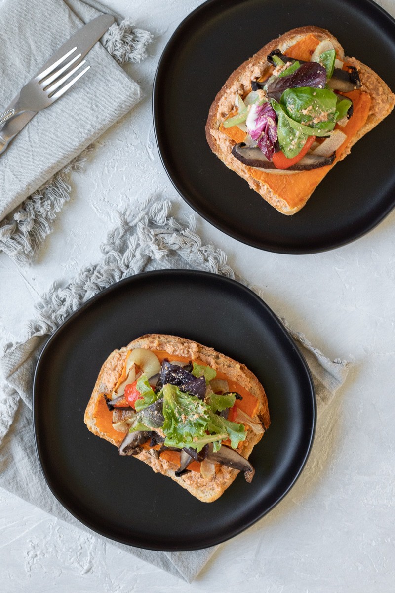 Two open face vegetable sandwiches on black plates.