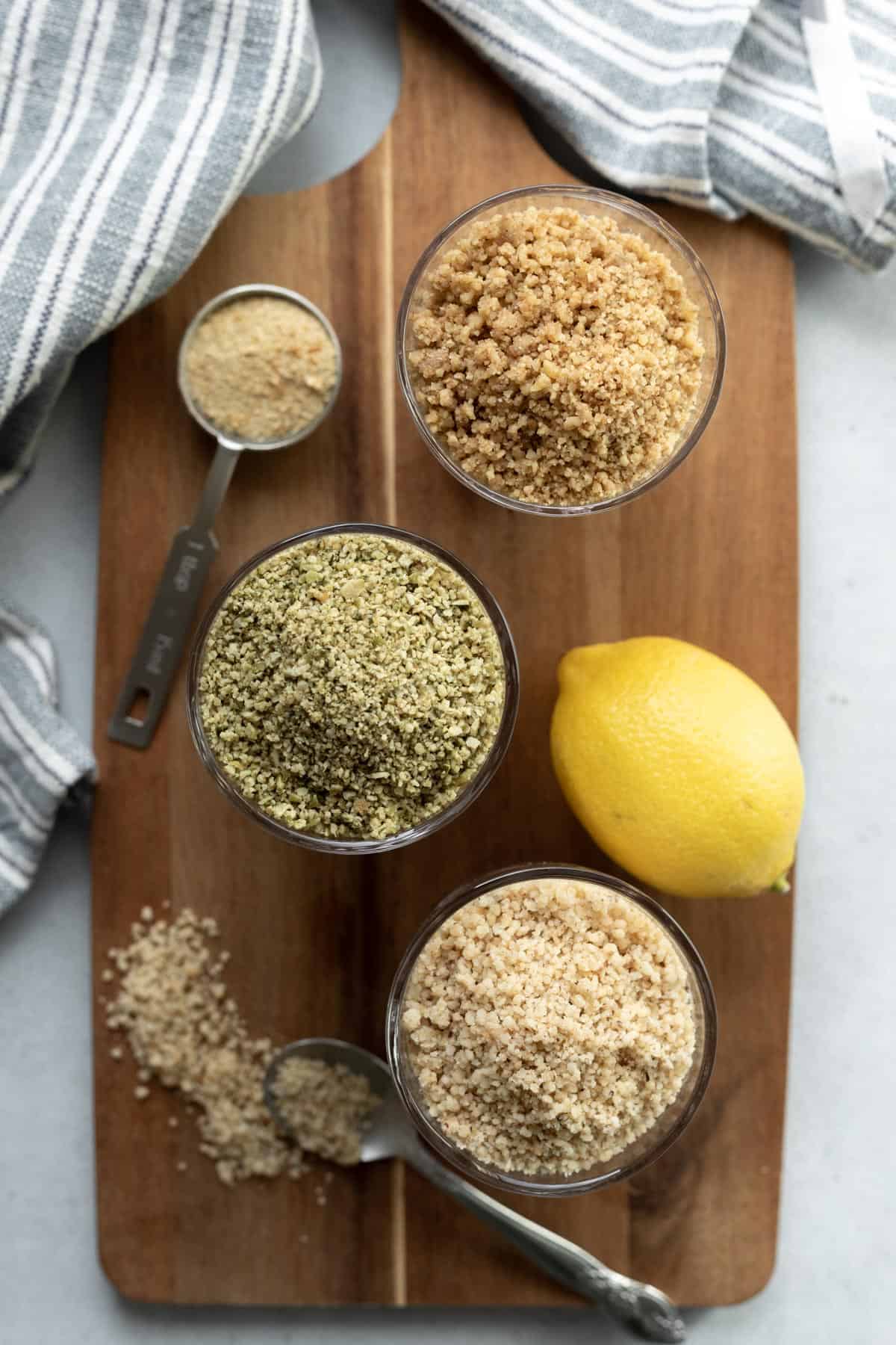 overhead photo of three different versions of vegan parmesan in glasses on a wood board.