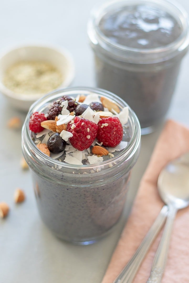 two servings of Berries and Greens Breakfast Pudding in glass jars topped with berries, coconut and almonds