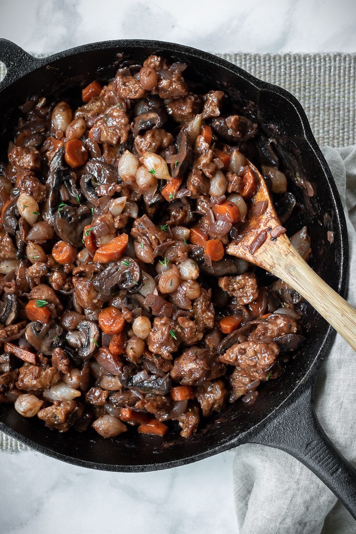 Chunky Vegan Beef Bourguignon in a cast iron skillet with a wooden spoon.