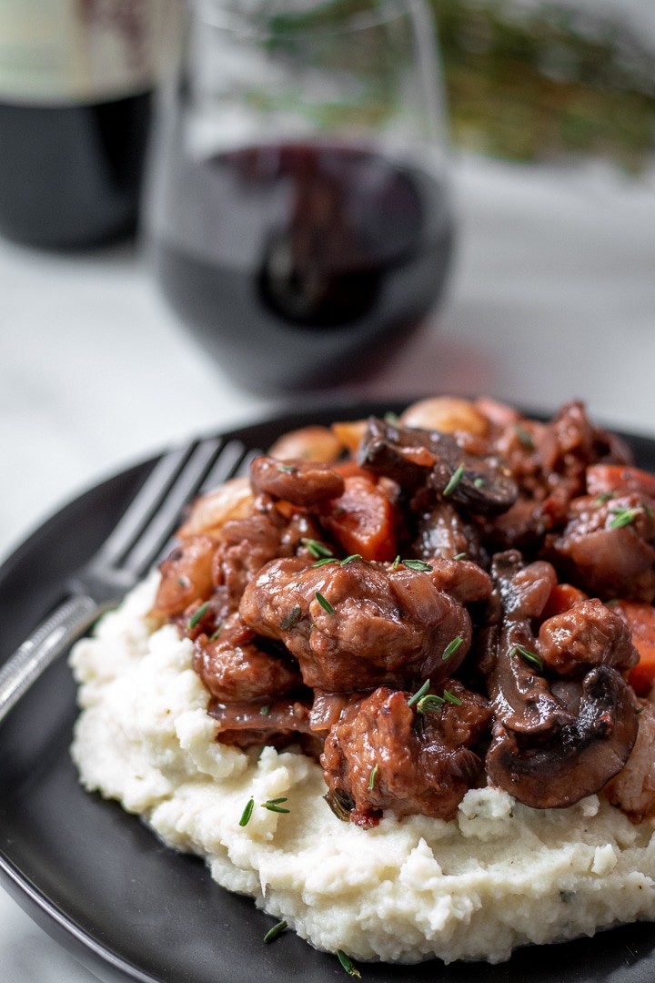 closeup photo of Seitan Bourguignon With Rosemary Cauliflower Mash on a black plate.