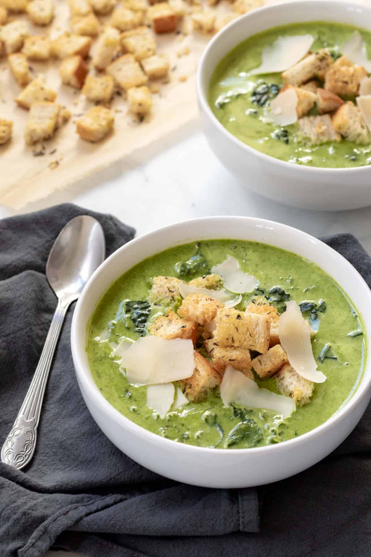 Two servings of Cream of Kale Soup in white bowls topped with homemade croutons.