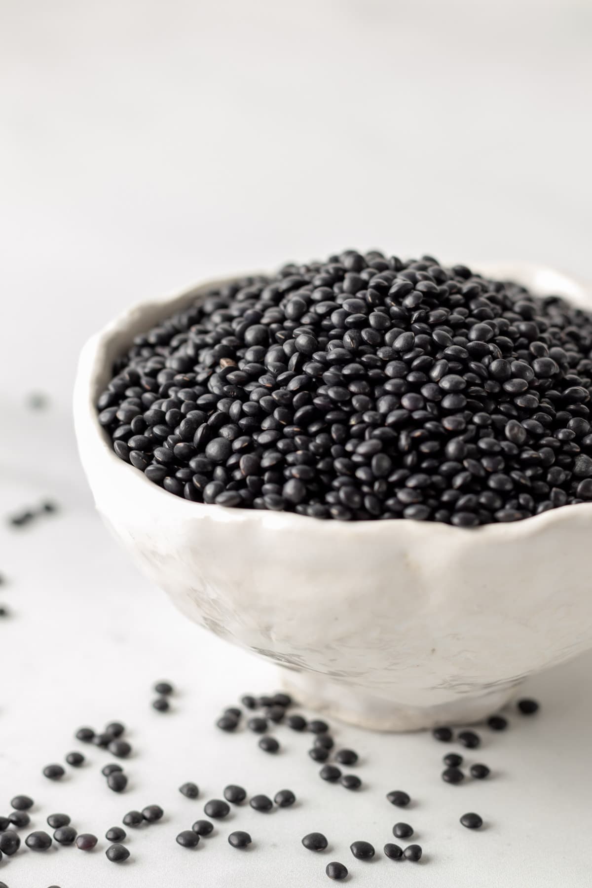 Dried black lentils in a small white bowl.