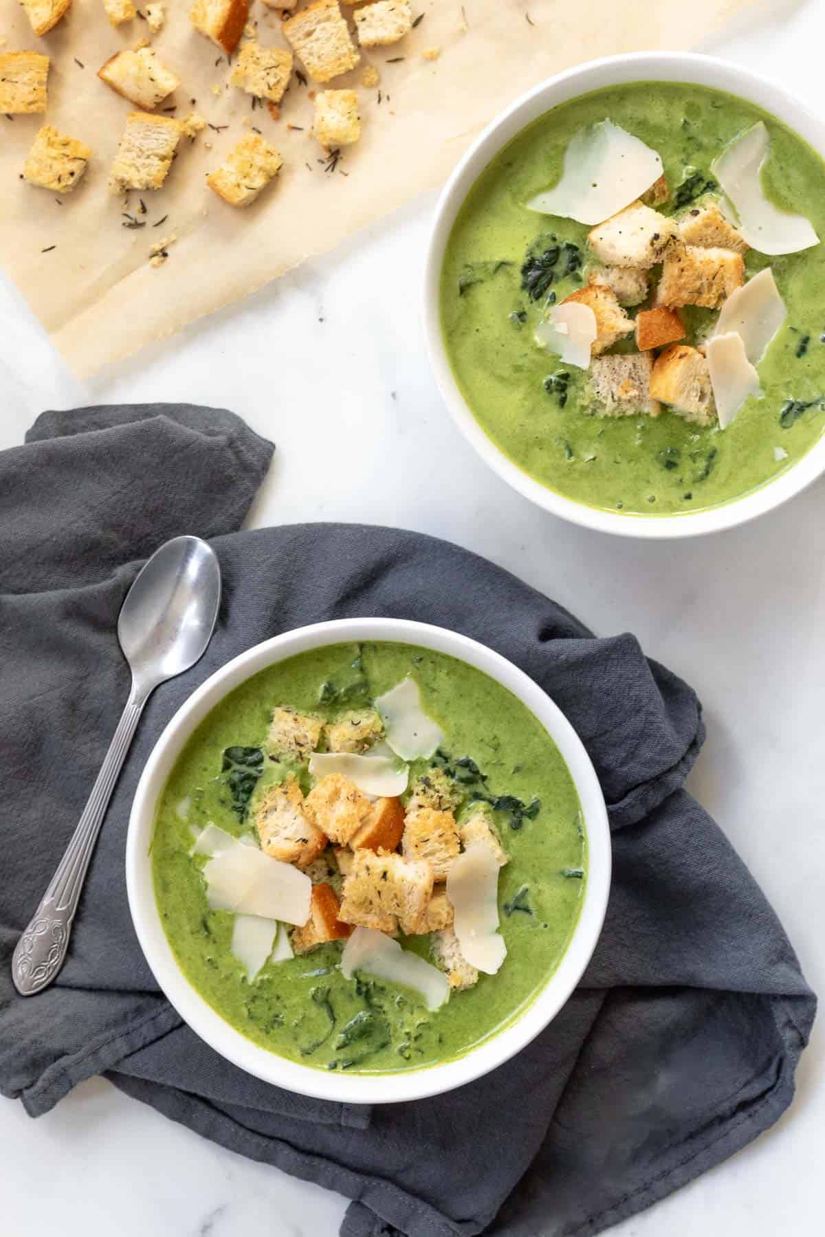 overhead shot of two bowls of Cream of Kale Soup with croutons.