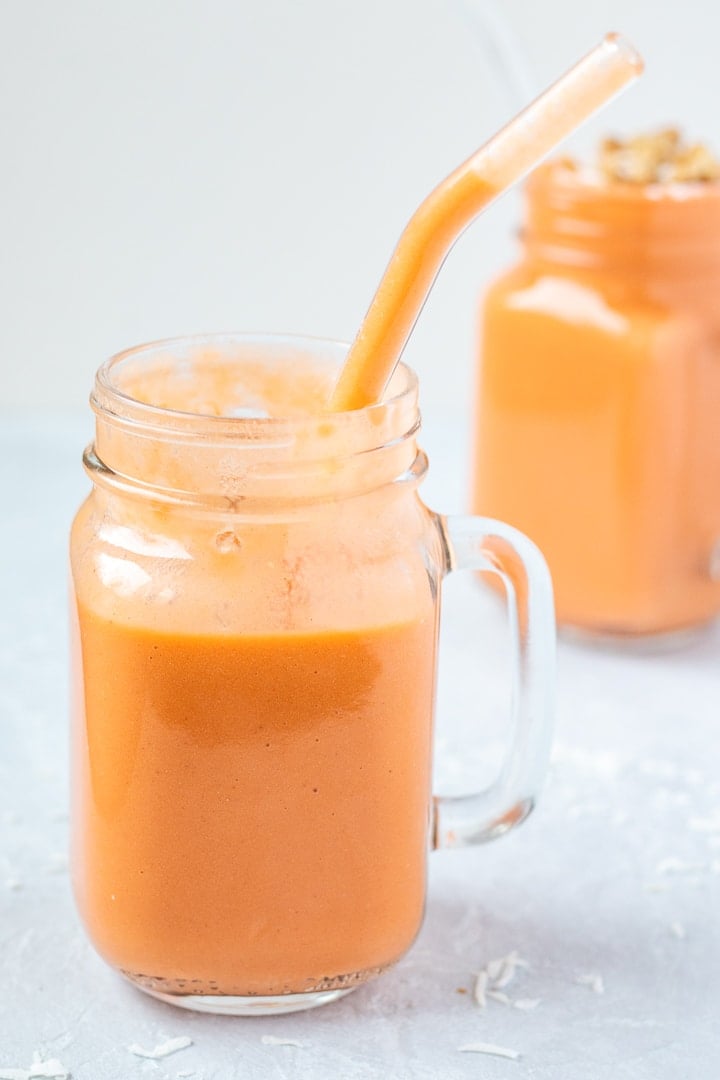 Creamy Carrot Banana Smoothie in a glass mug with a glass straw.