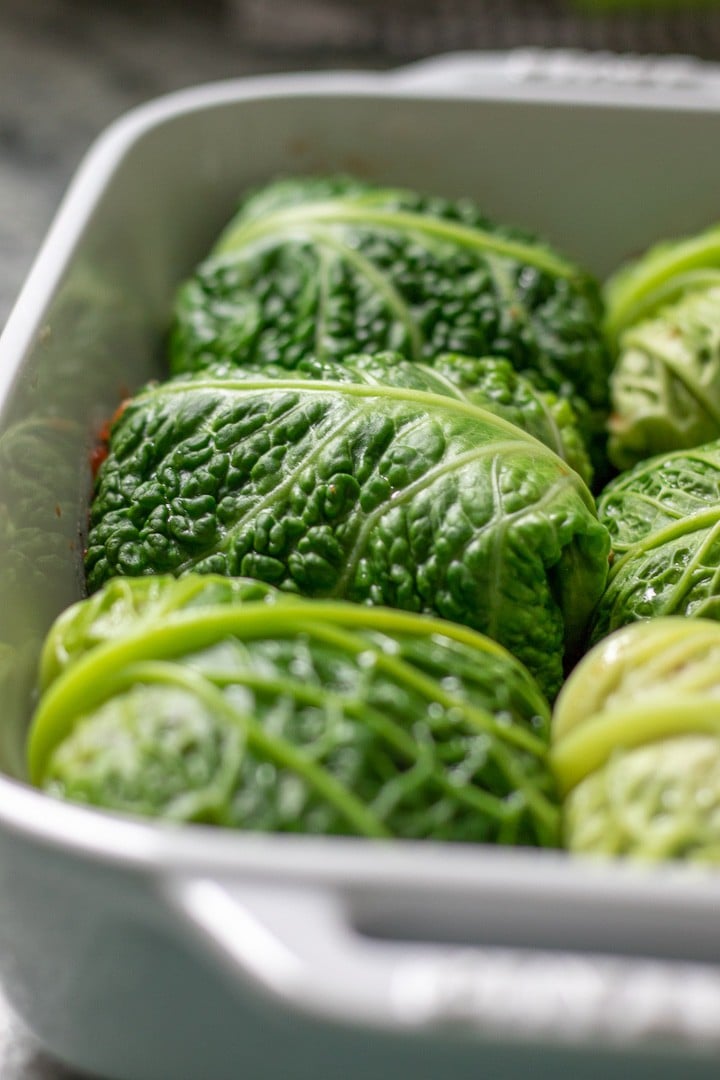 Vegan savoy cabbage rolls in white baking dish.