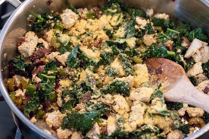 Sautéing vegetables in a pan with tofu and nutritional yeast.