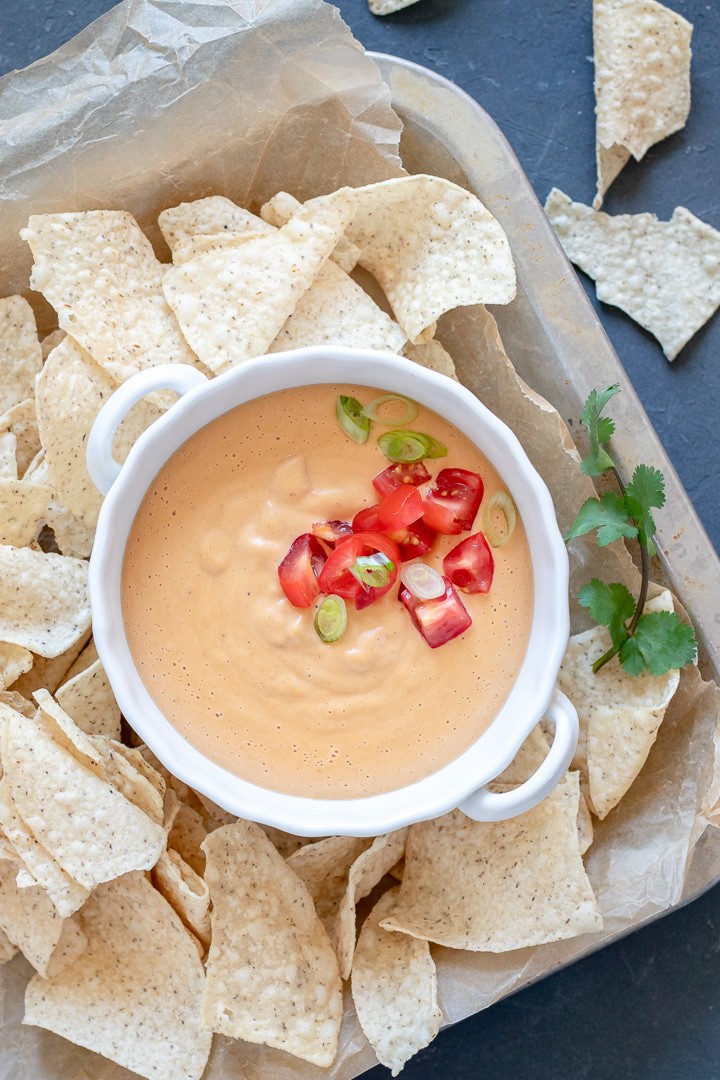 bowl of queso on a platter surrounded by tortilla chips