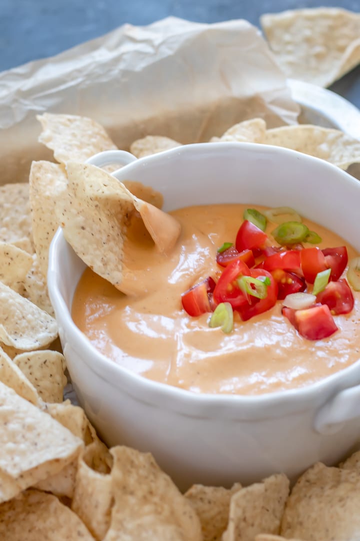 close up of tortilla chip in bowl of vegan queso