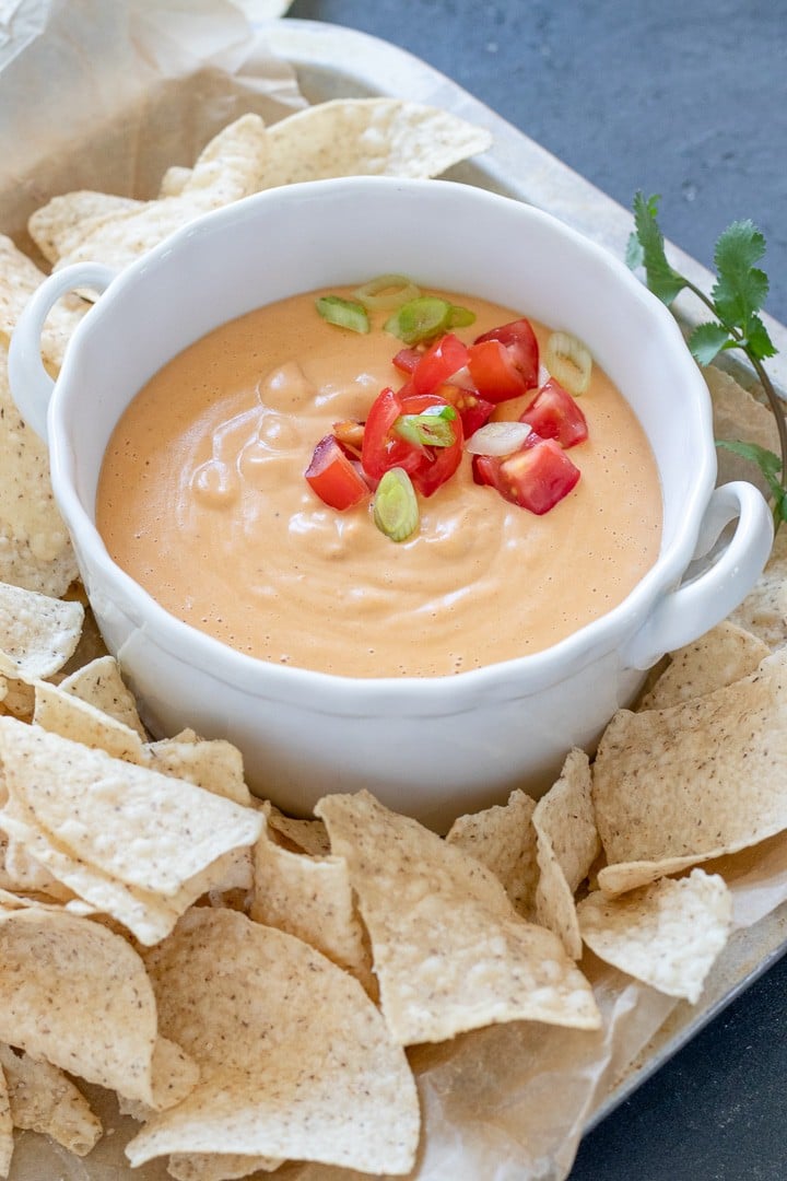 Vegan Queso in a white bowl topped with tomato and green onion.