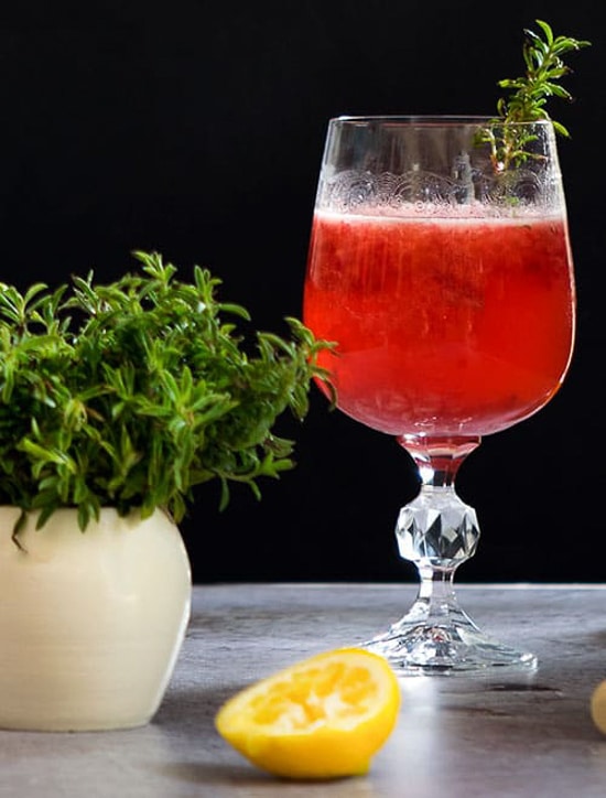 Raspberry thyme cocktail in a glass with fresh lemon and thyme.