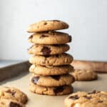 A stack of Spelt Cookies filled with chocolate chips and peanuts on a baking sheet.