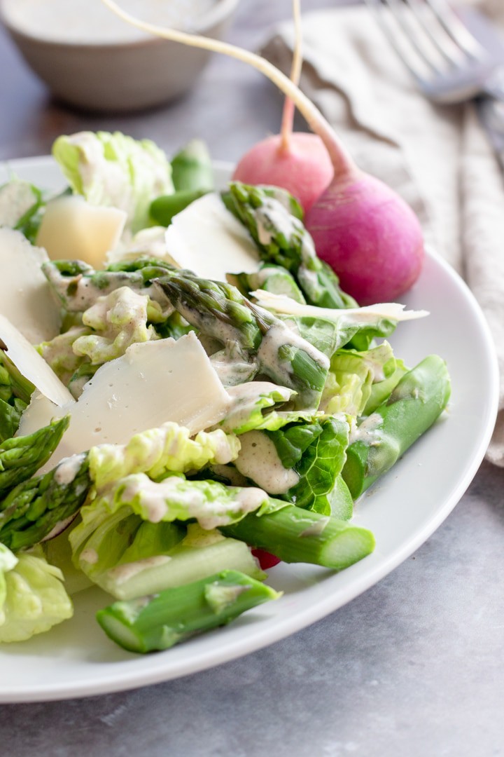 asparagus salad on a white plate with two Easter egg radishes.