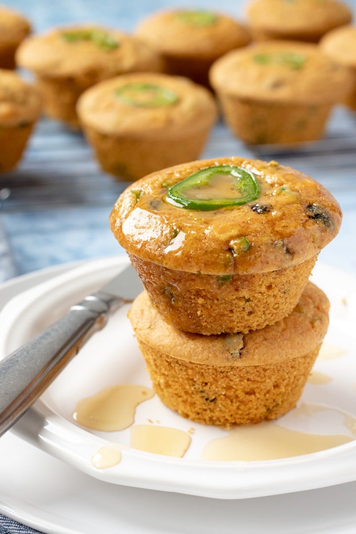 Two vegan cornbread muffins stacked, topped with melted butter and maple syrup.