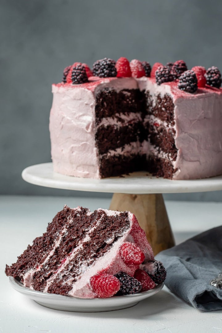 Vegan Chocolate Layer Cake on a cake stand and a slice on a plate.