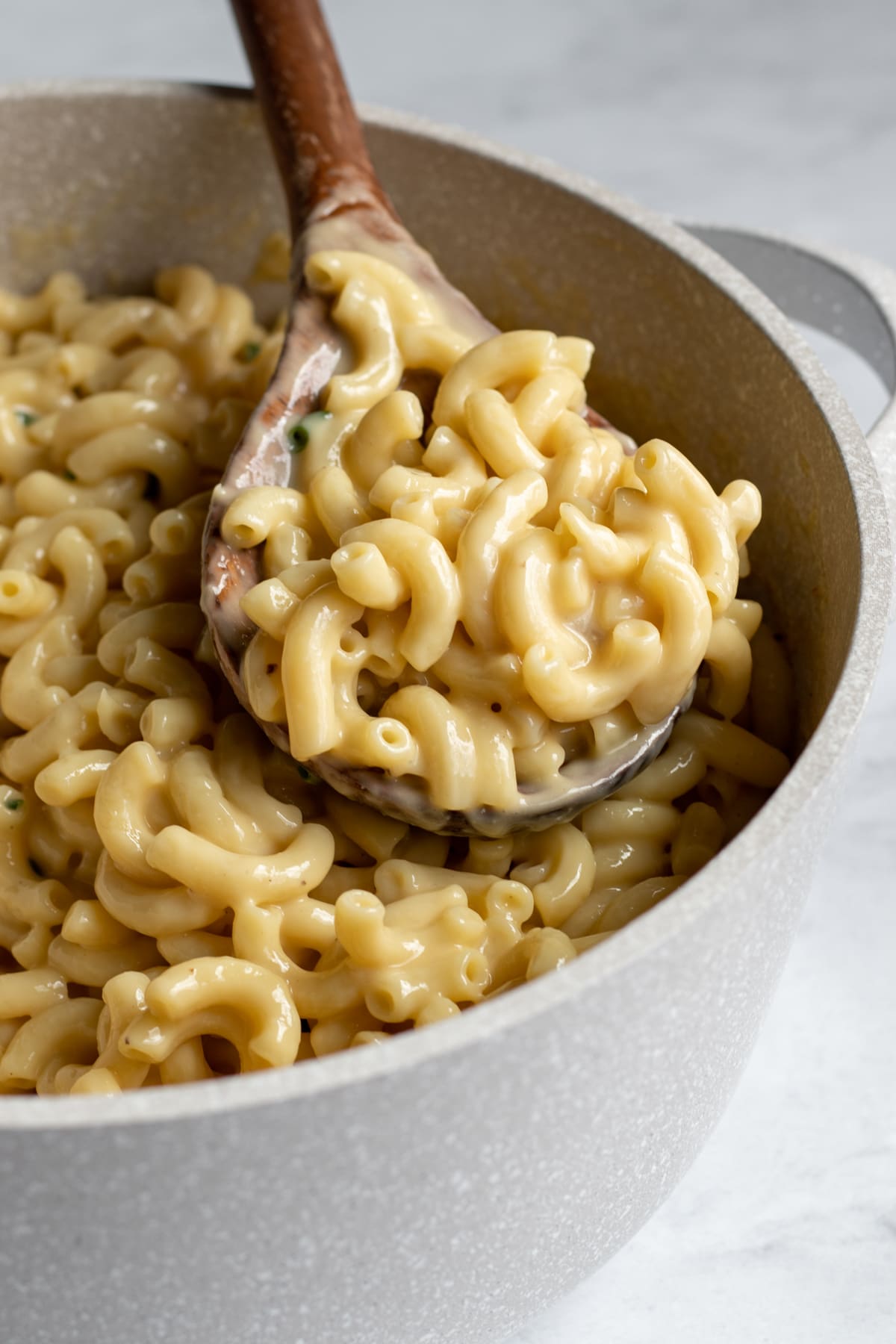 large wooden serving spoon scooping up vegan macaroni and cheese from a pot.