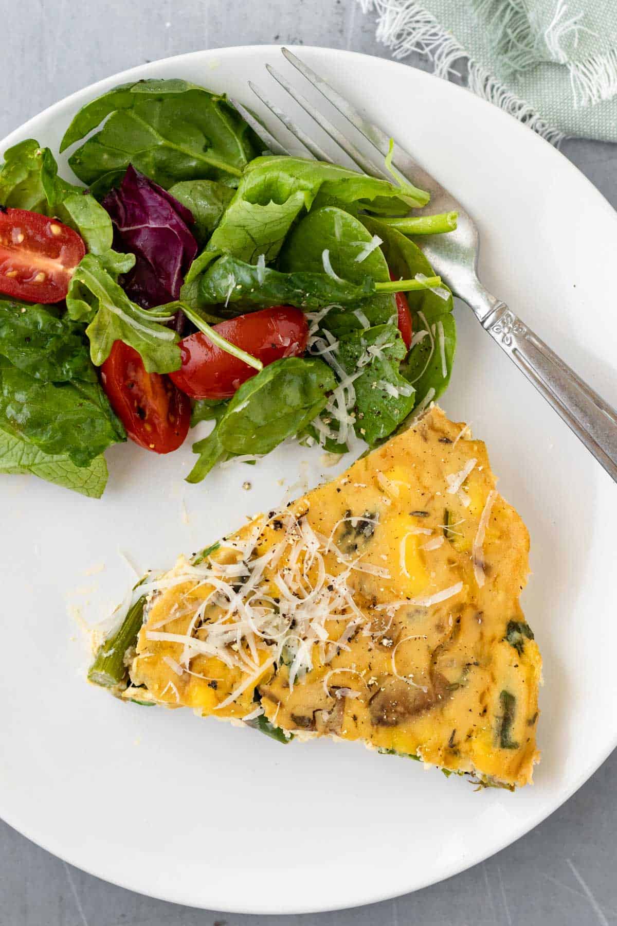 a slice of vegan quiche on a white plate with shaved Parm and side salad.