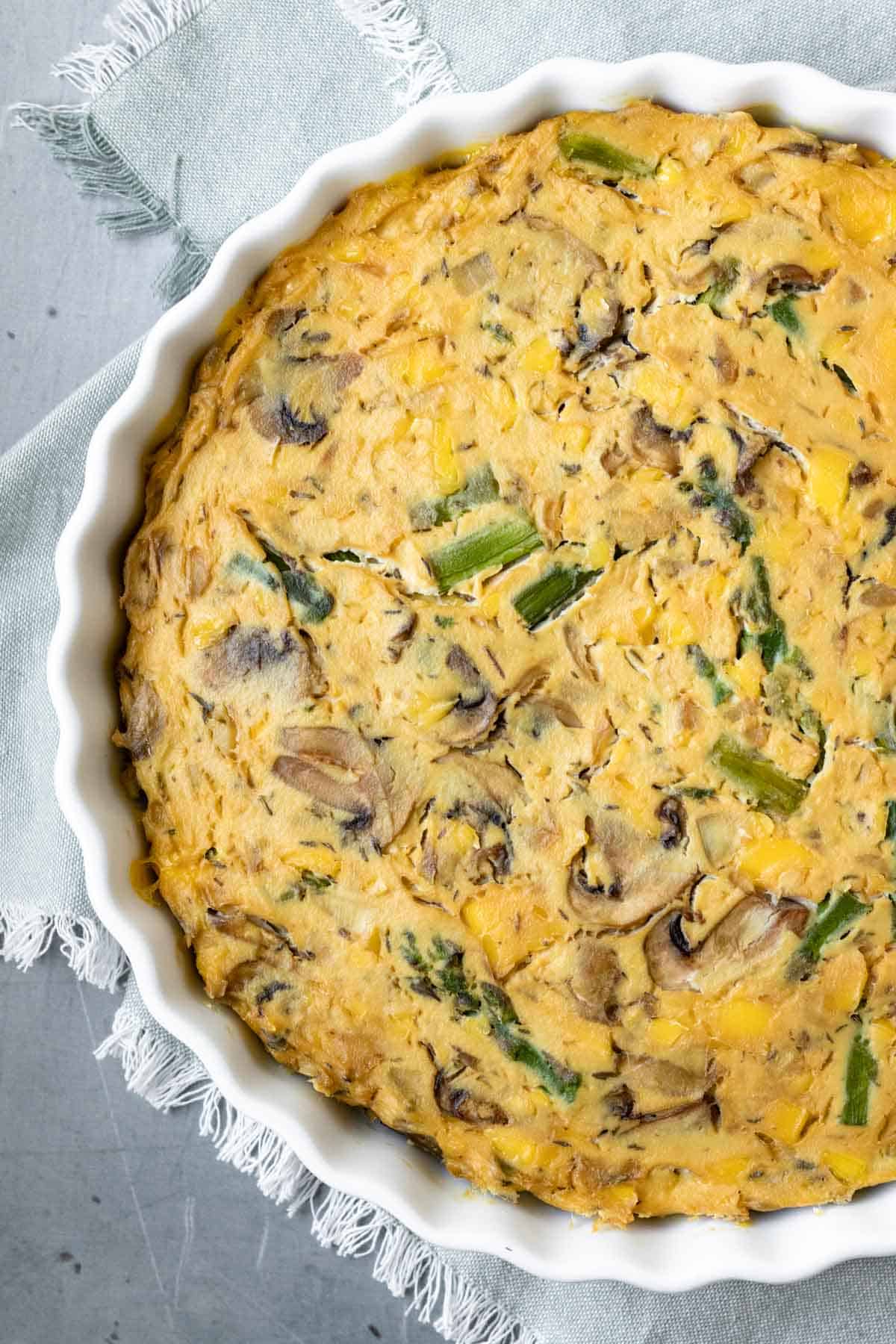 overhead view of whole vegan quiche with asparagus and cheese in a white pie plate.