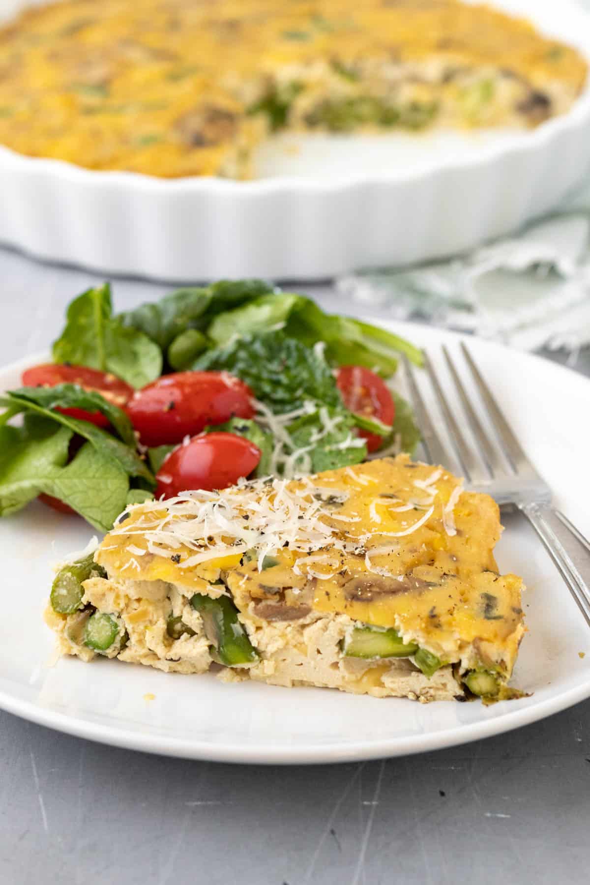 a slice of tofu quiche with side salad on a white plate .