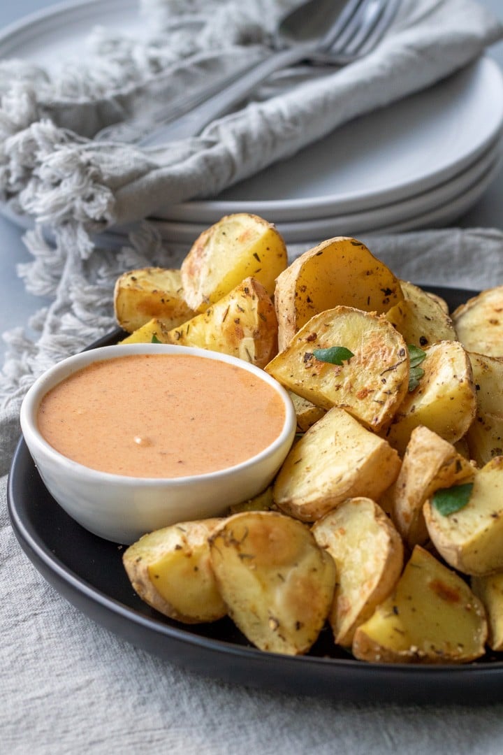 roasted potatoes on a black plate with a bowl of harissa dressing on the side.