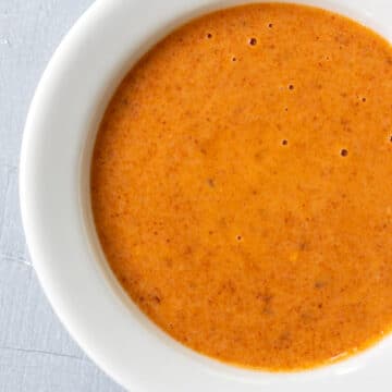 Vibrant orange harissa dressing in a white bowl