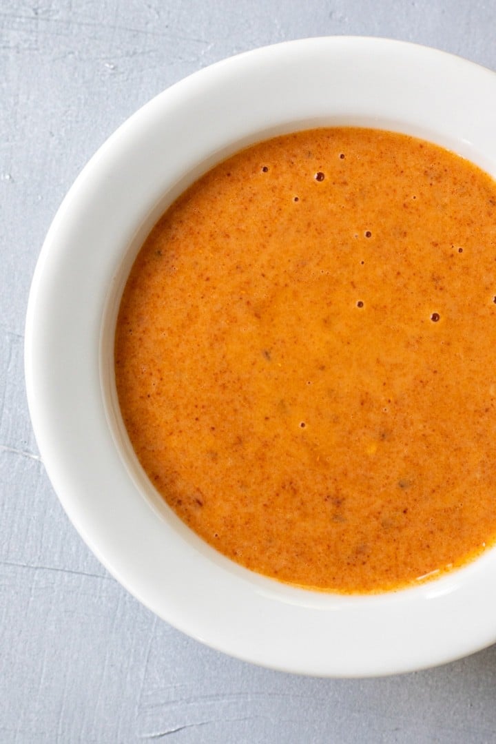 Vibrant orange harissa dressing in a white bowl.