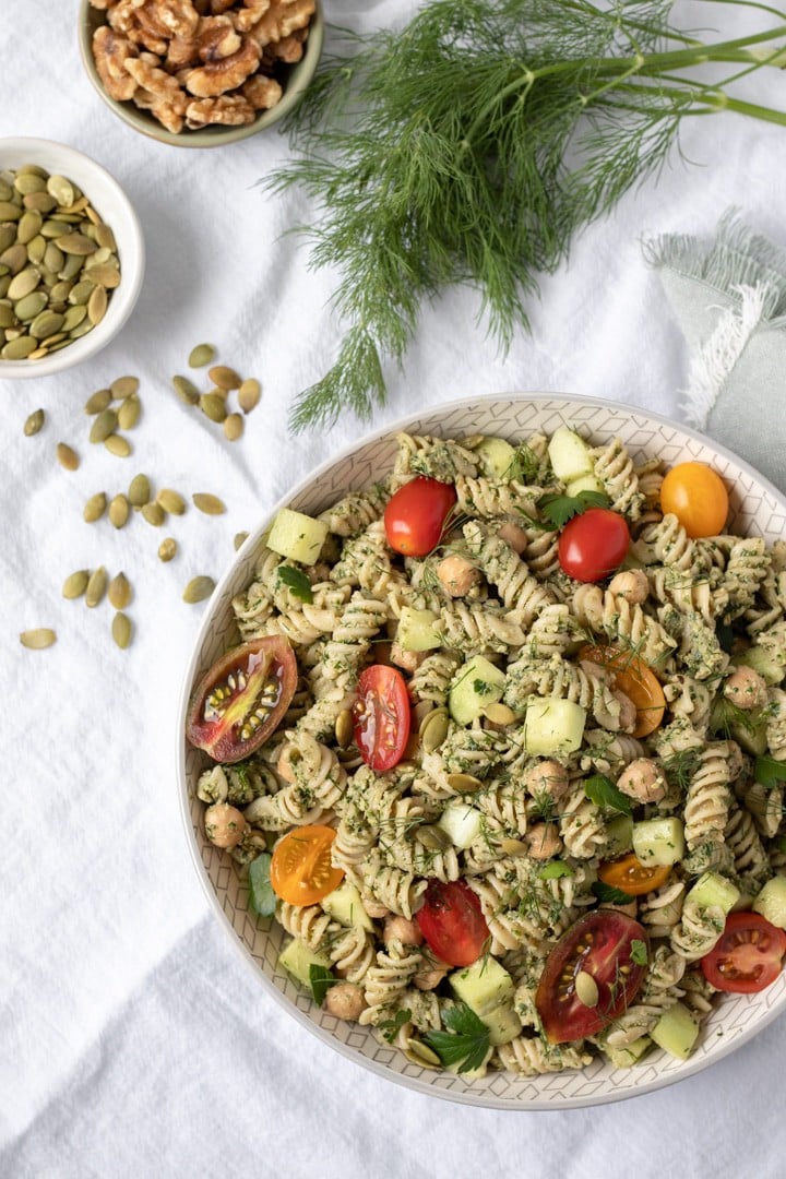 Colorful pasta salad with dill pesto, tomatoes and cucumbers in a white bowl.