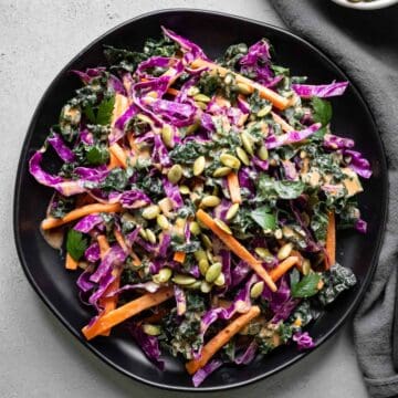 Vibrant and colorful slaw with kale, red cabbage, and carrot on a black plate.