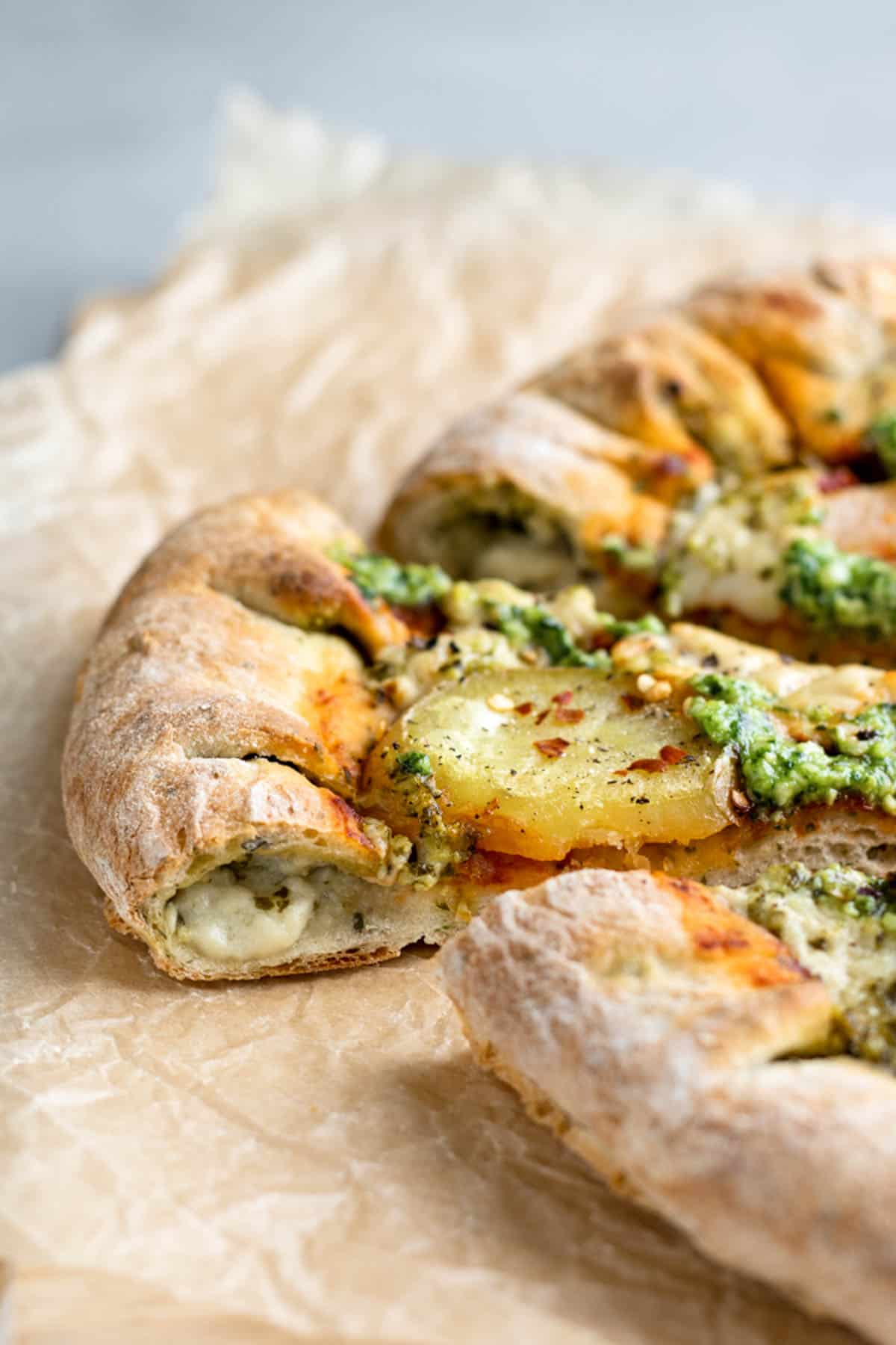 side view of vegan pesto pizza with cheese and pesto oozing out of the stuffed crust.